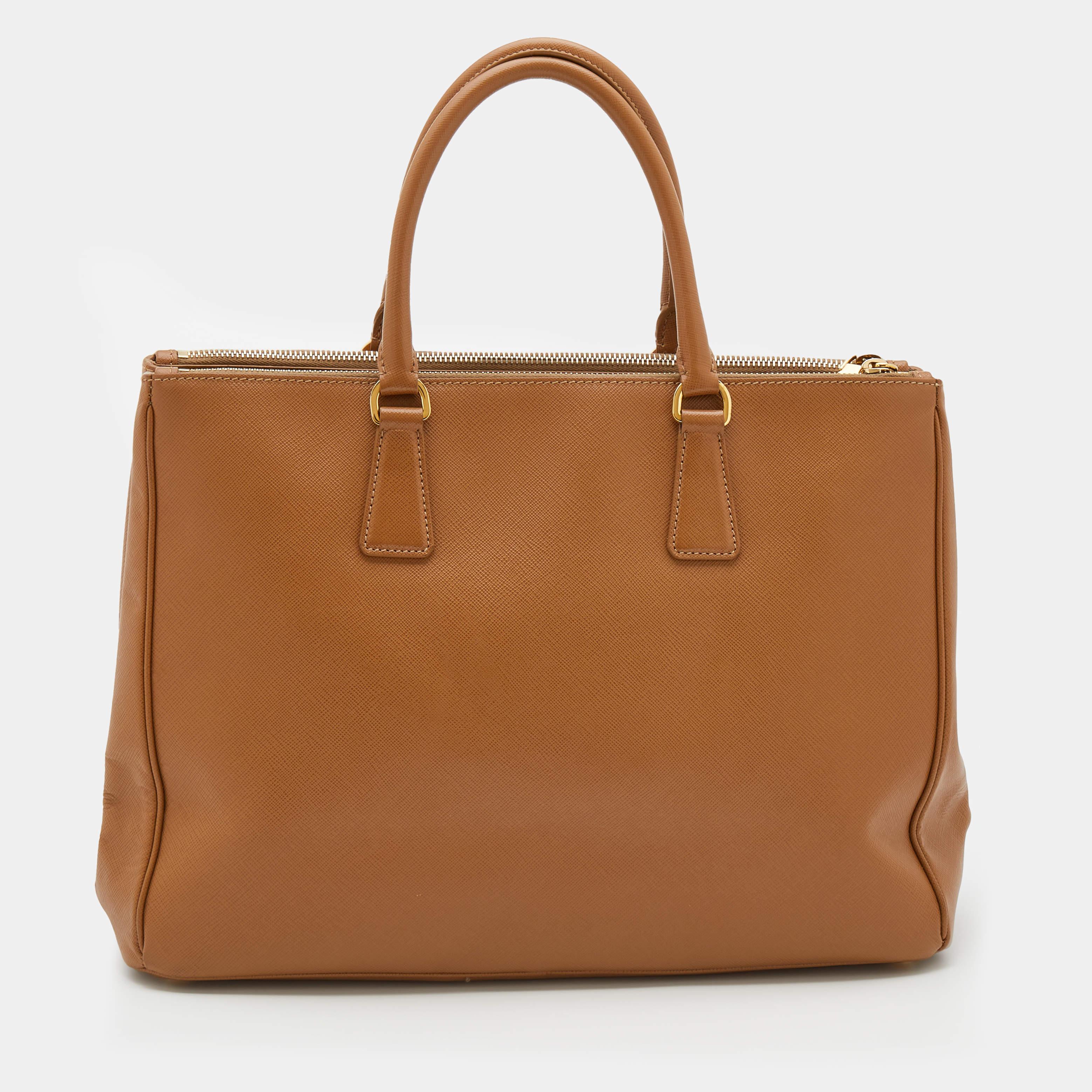 Feminine in shape and grand in design, this Double Zip tote by Prada will be a loved addition to your closet. It has been crafted from Saffiano Lux leather and styled minimally with gold-tone hardware. It comes with two top handles, two zip