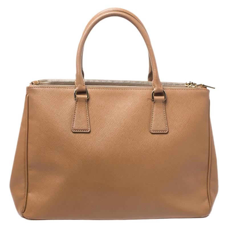 Feminine in shape and grand in design, this Double Zip tote by Prada will be a loved addition to your closet. It has been crafted from Saffiano Lux leather and styled minimally with gold-tone hardware. It comes with two top handles, two zip