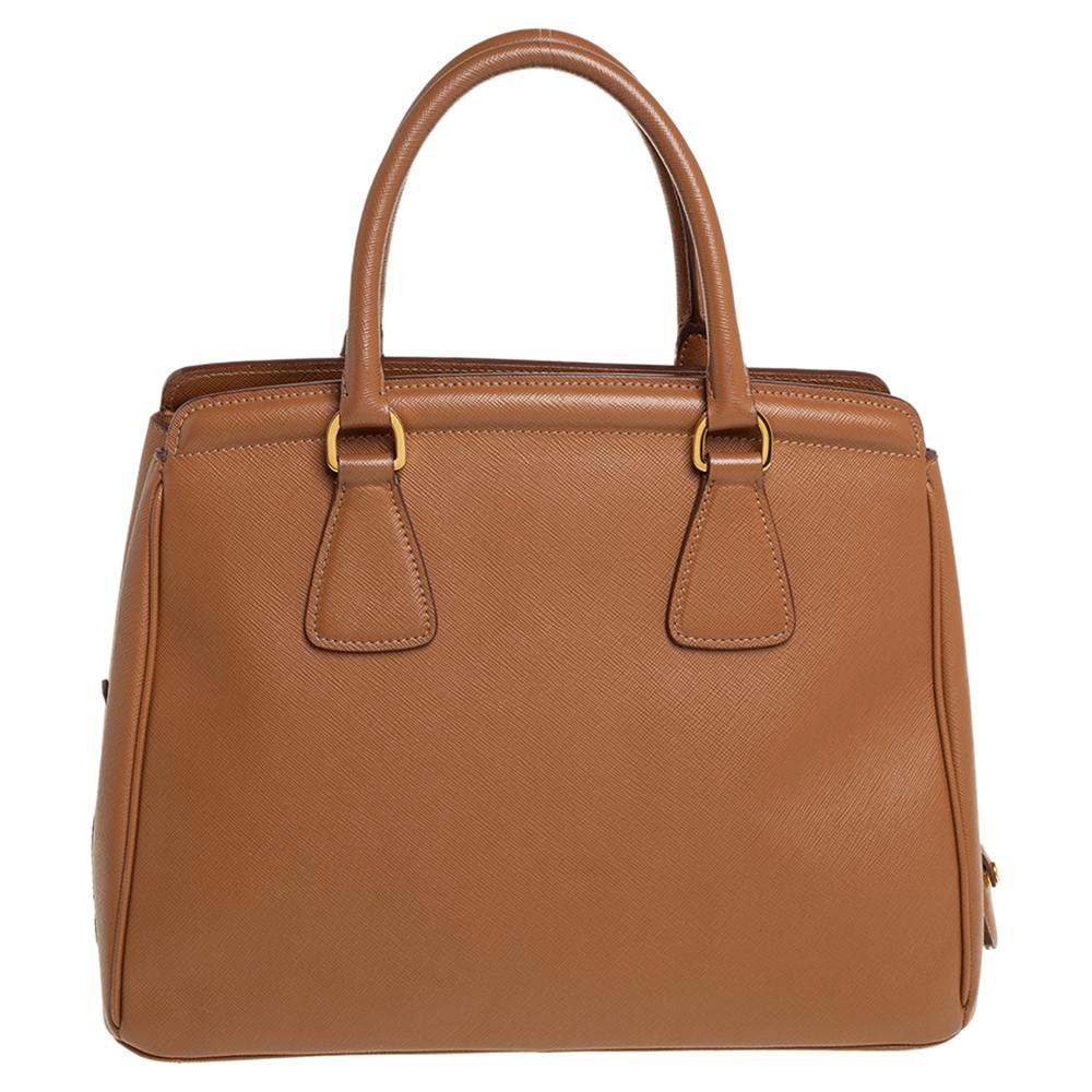 Meticulously created, this Parabole tote by Prada is a style statement in itself. Designed from Saffiano Lux leather into a sturdy shape, it exudes style and class in equal measures. This delightful caramel-hued piece is held by two top handles and