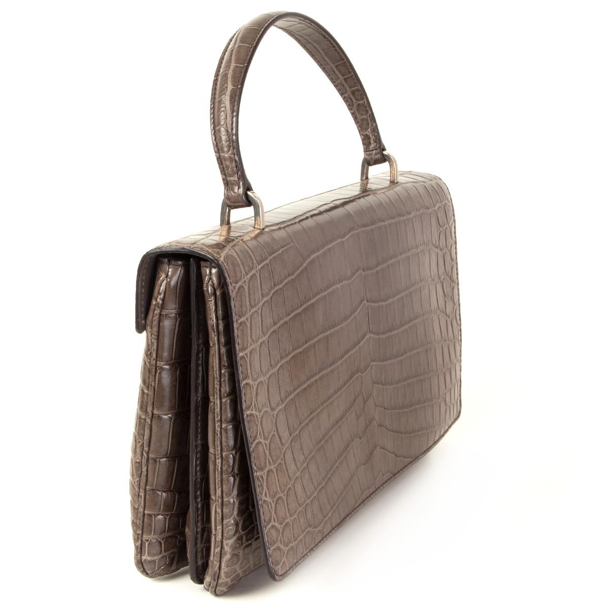 100% authentic Prada 1BA017 handbag in ash/cenere crocodile with silver-tone hardware. Opens with a magnetic button under the flap and is lined in ash lambskin. The interior is divided in three compartements with one zipper pocket against the back,