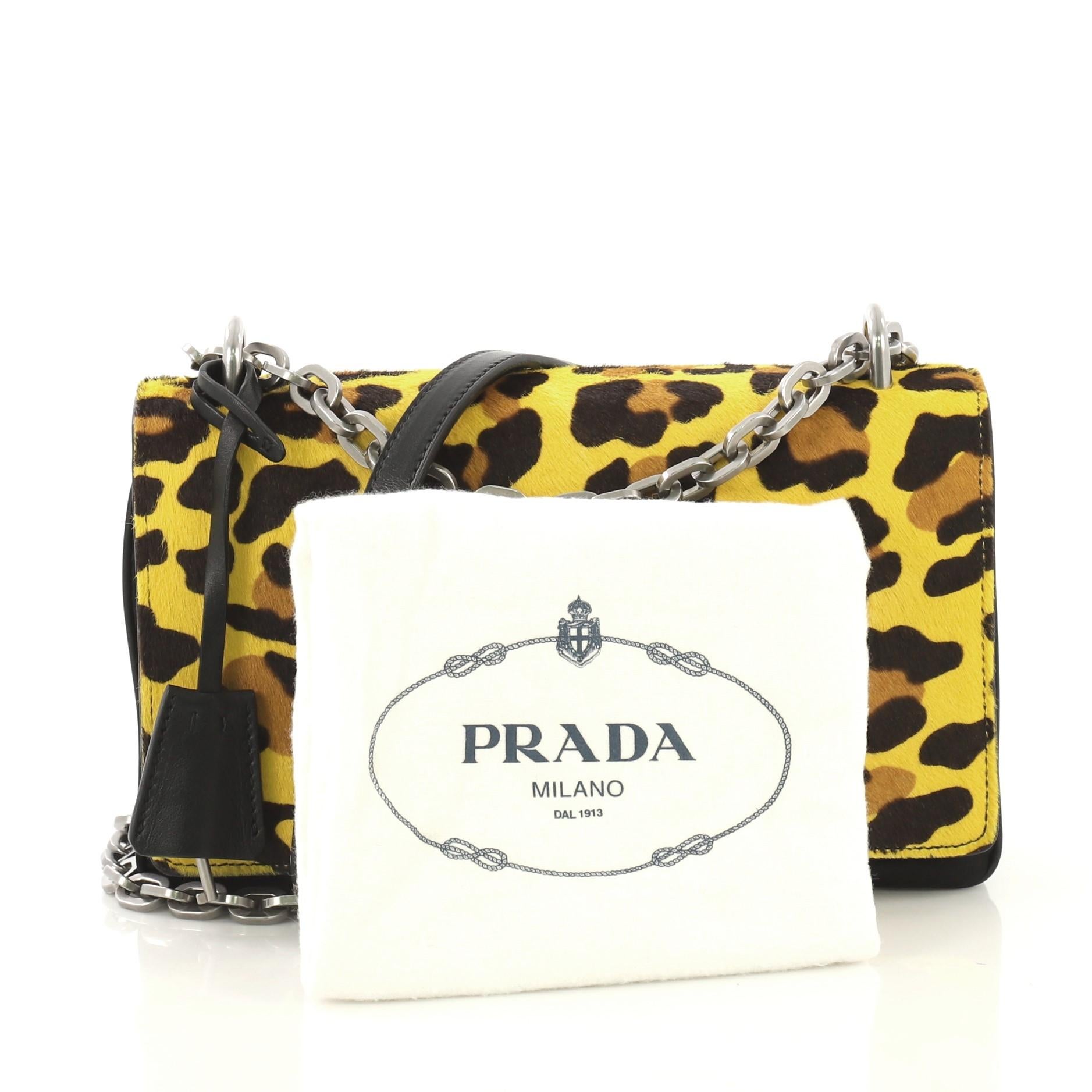 This Prada Chain Flap Shoulder Bag Pony Hair and Nylon Medium, crafted from yellow printed pony hair and black nylon, features chain link shoulder strap, frontal flap, accordion sides, and silver-tone hardware. Its metal closure opens to a black