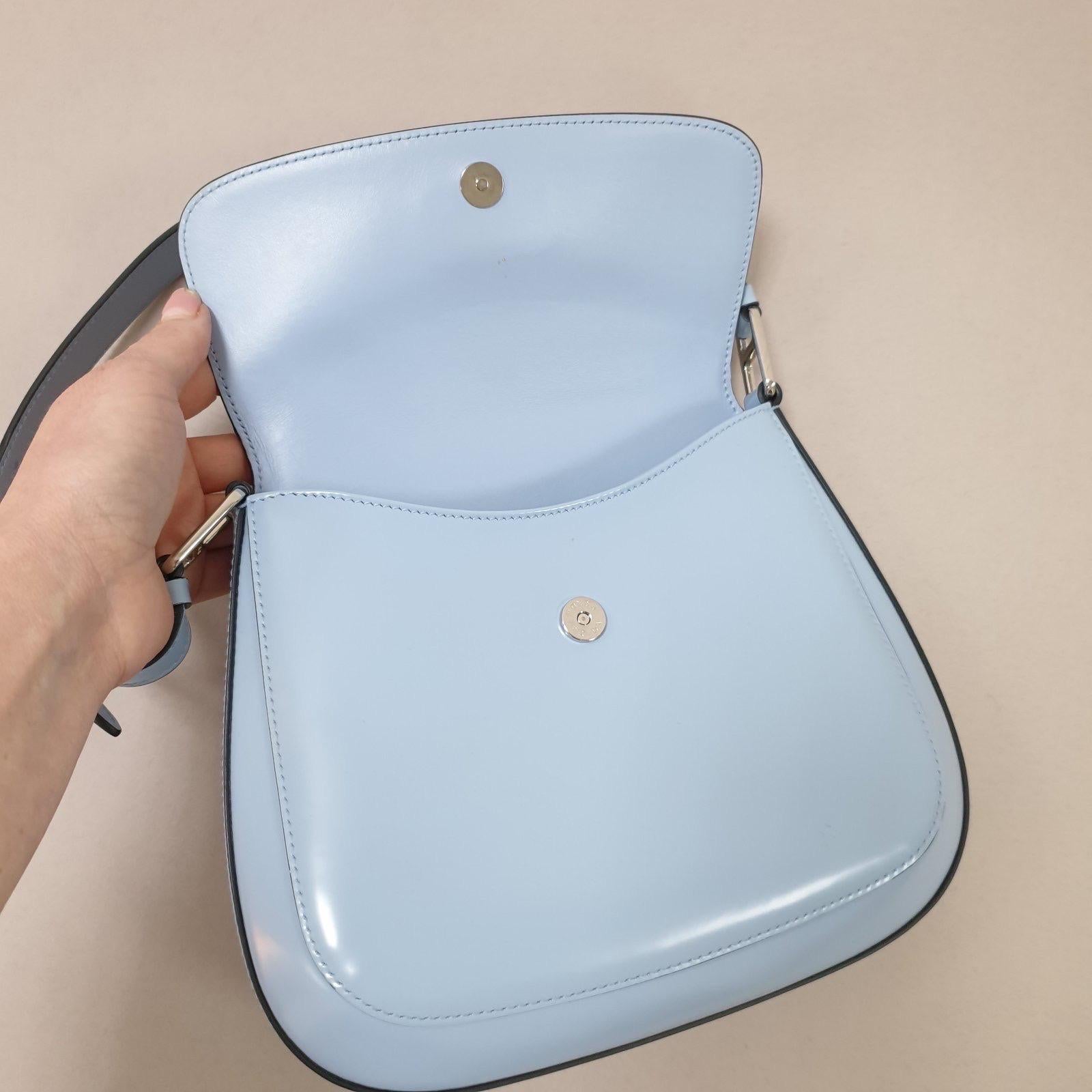 This Prada Cleo shoulder bag is made from blue brushed leather with silver tone hardware. 
Details include a flat handle, back open pocket, and magnetic snap closure. 
The interior is fully lined with one open pocket.
Measurements:
26 x 21 x 5