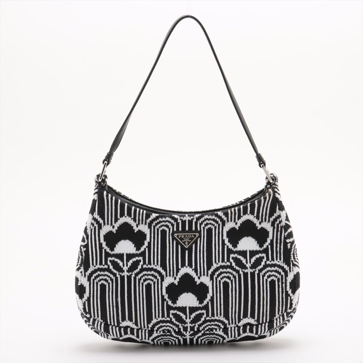 The Prada Cleo Jacquard Shoulder Bag in Black and White is a stylish and modern accessory that exudes sophistication. Featuring the brand’s signature jacquard fabric, the bag showcases a striking black and white floral pattern with a sleek, curved