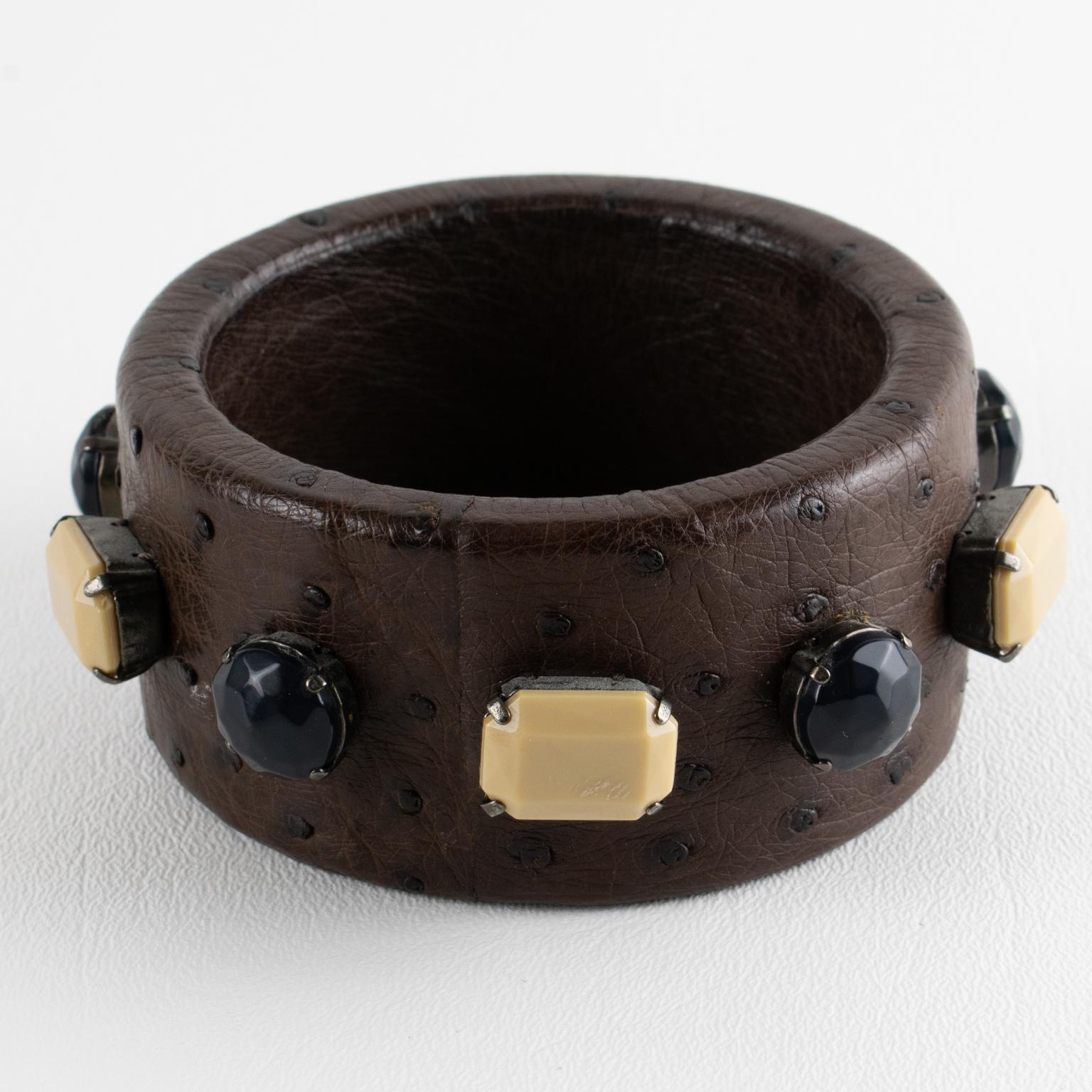 Prada, Italia, ha disegnato questo splendido braccialetto bangle in pelle. Questo straordinario accessorio di moda combina il fascino lussuoso della pelle di struzzo marrone cacao con gli accenti misteriosi degli strass in resina neri e bianco
