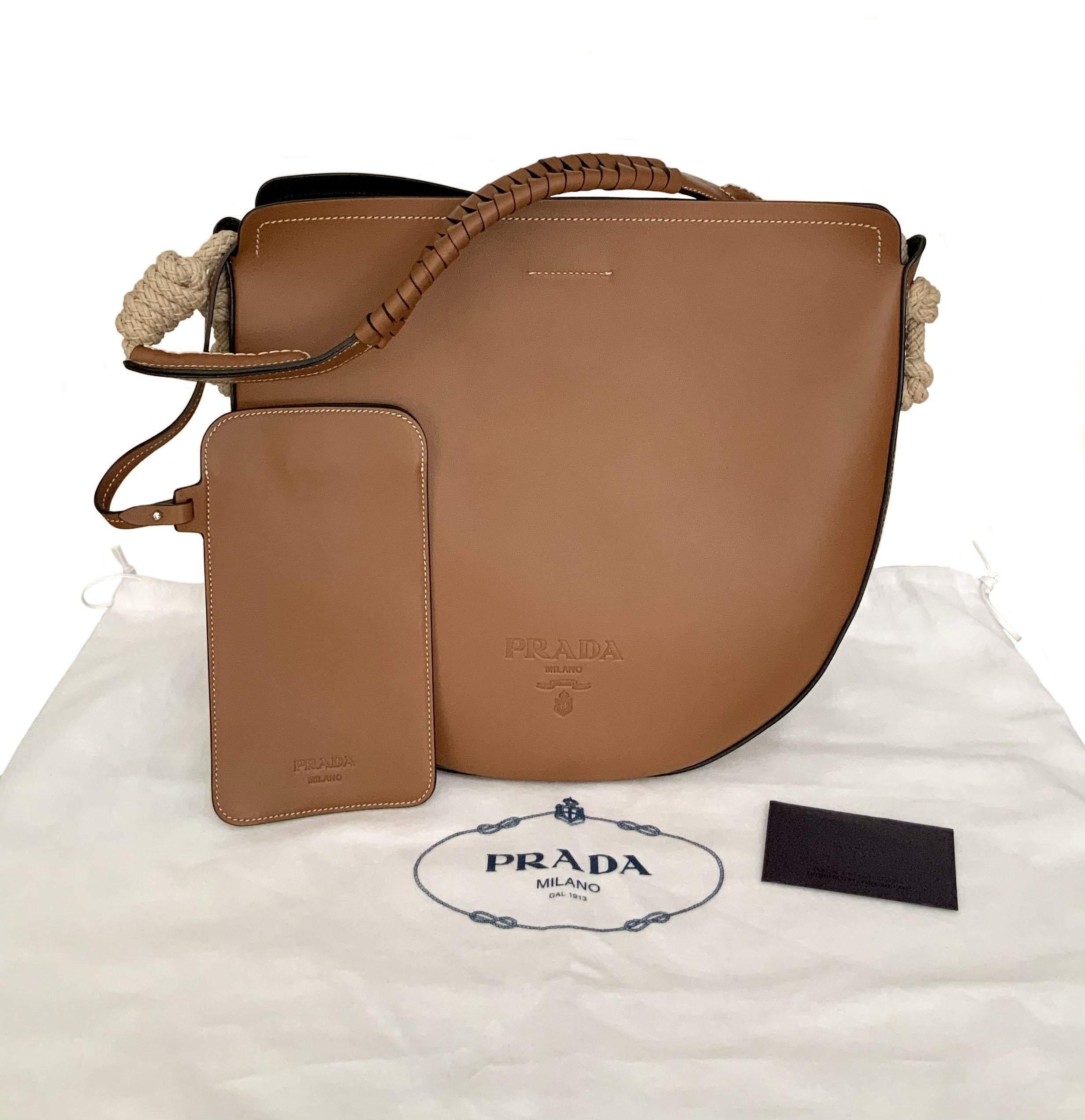 This pre-owned but new bag from the house of Prada is crafted in calfskin leather with contrasting cord details. 
It features a woven handle, the iconic hot-pressed logo on the front and a black Nappa leather interior.
A magnet closure and a