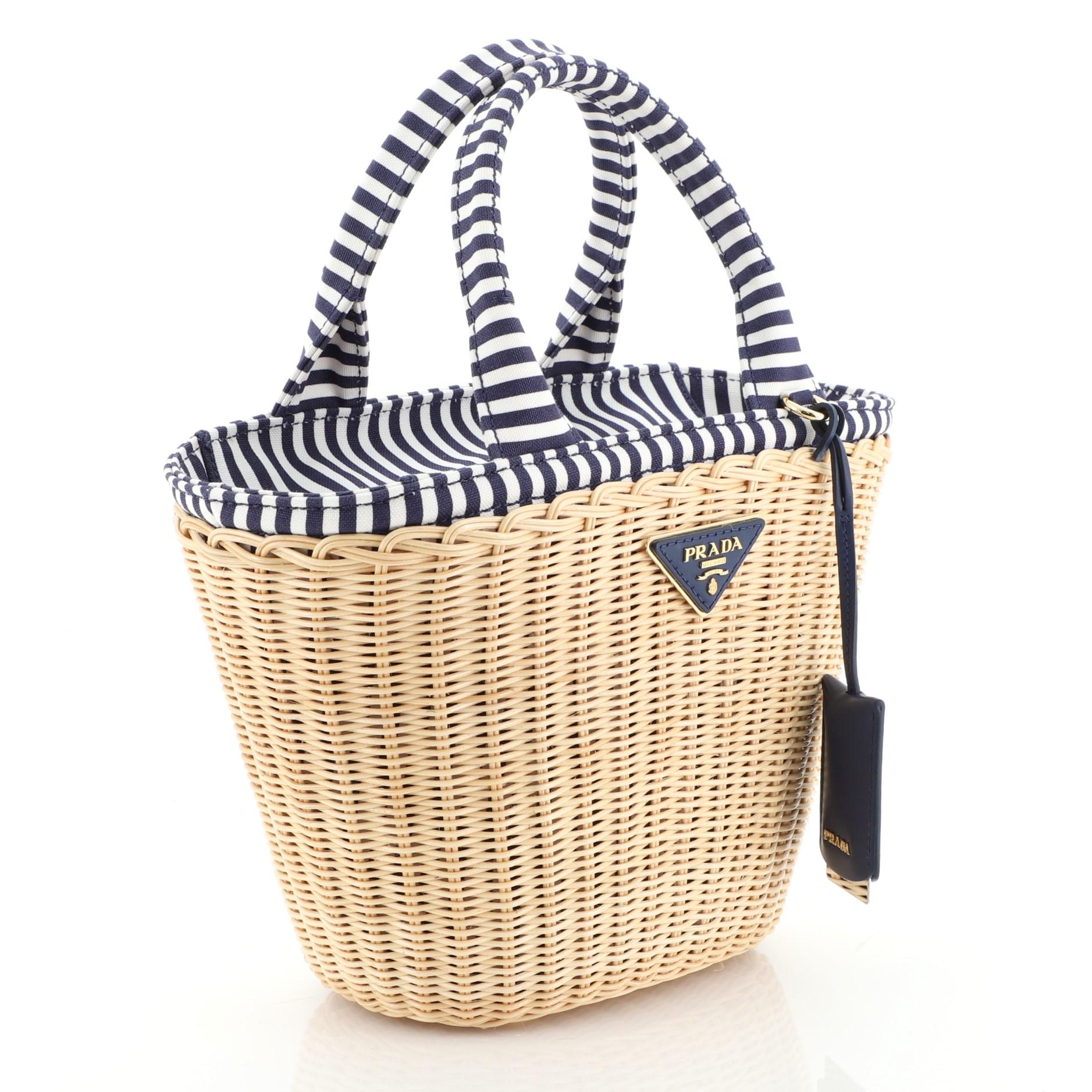 This Prada Convertible Basket Bag Wicker with Canvas Small, crafted from neutral wicker with canvas, features dual rolled handles, triangle Prada logo, and gold-tone hardware. Its zip closure opens to a blue printed fabric interior. 

Estimated