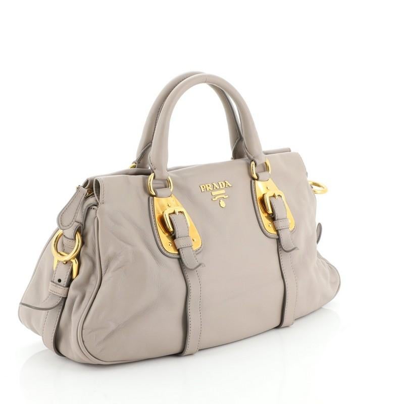 This Prada Convertible Belted Satchel Soft Calfskin Medium, crafted from neutral soft calfskin leather, features belted sides and front, dual rolled leather handles, Prada Milano logo, and gold-tone hardware. Its top zip closure opens to a neutral