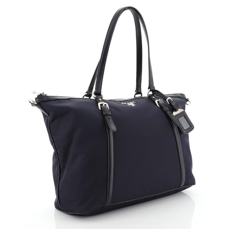 This Prada Convertible Belted Tote Tessuto Medium, crafted from blue tessuto nylon, features dual tall flat leather handles with belt and buckle details, silver-tone raised Prada logo, protective base studs, and silver-tone hardware accents. Its zip
