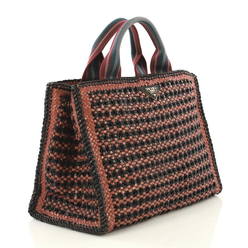 This Prada Convertible Open Tote Madras Woven Leather Medium, crafted in brown and black woven leather, features dual top handles, Prada triangle logo, protective base studs and gold-tone hardware. Its snap button closure opens to a burgundy fabric