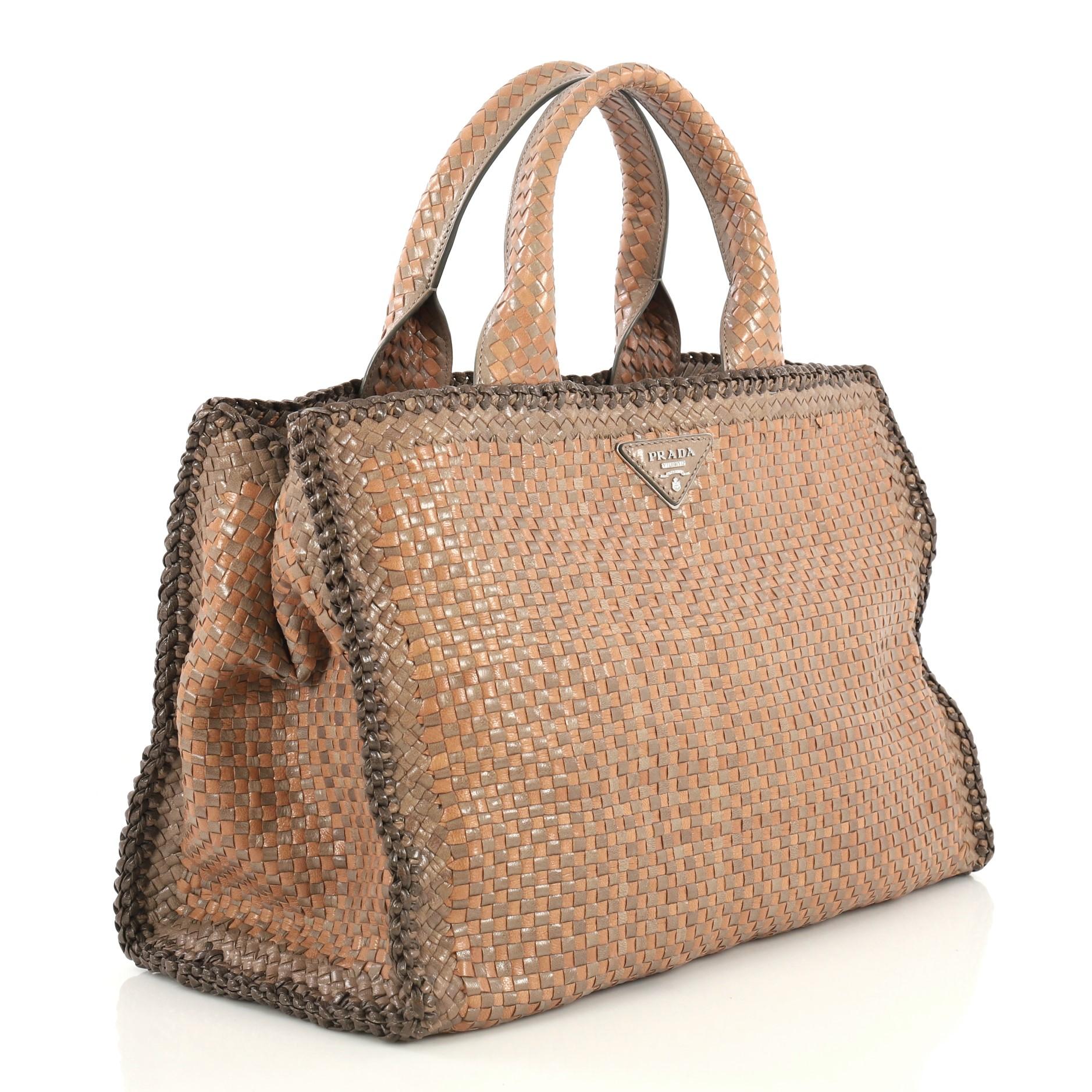This Prada Convertible Open Tote Madras Woven Leather Medium, crafted in neutral madras woven leather, features dual top handles, Prada triangle logo on front, protective base studs, and silver-tone hardware. Its snap button closure opens to a gray