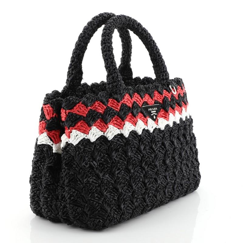 This Prada Convertible Open Tote Woven Raffia Mini, crafted in black multicolor raffia, features dual woven handles, Prada triangle logo, and silver-tone hardware. Its snap button closure opens to a black fabric interior.  

Condition: Great. Slight