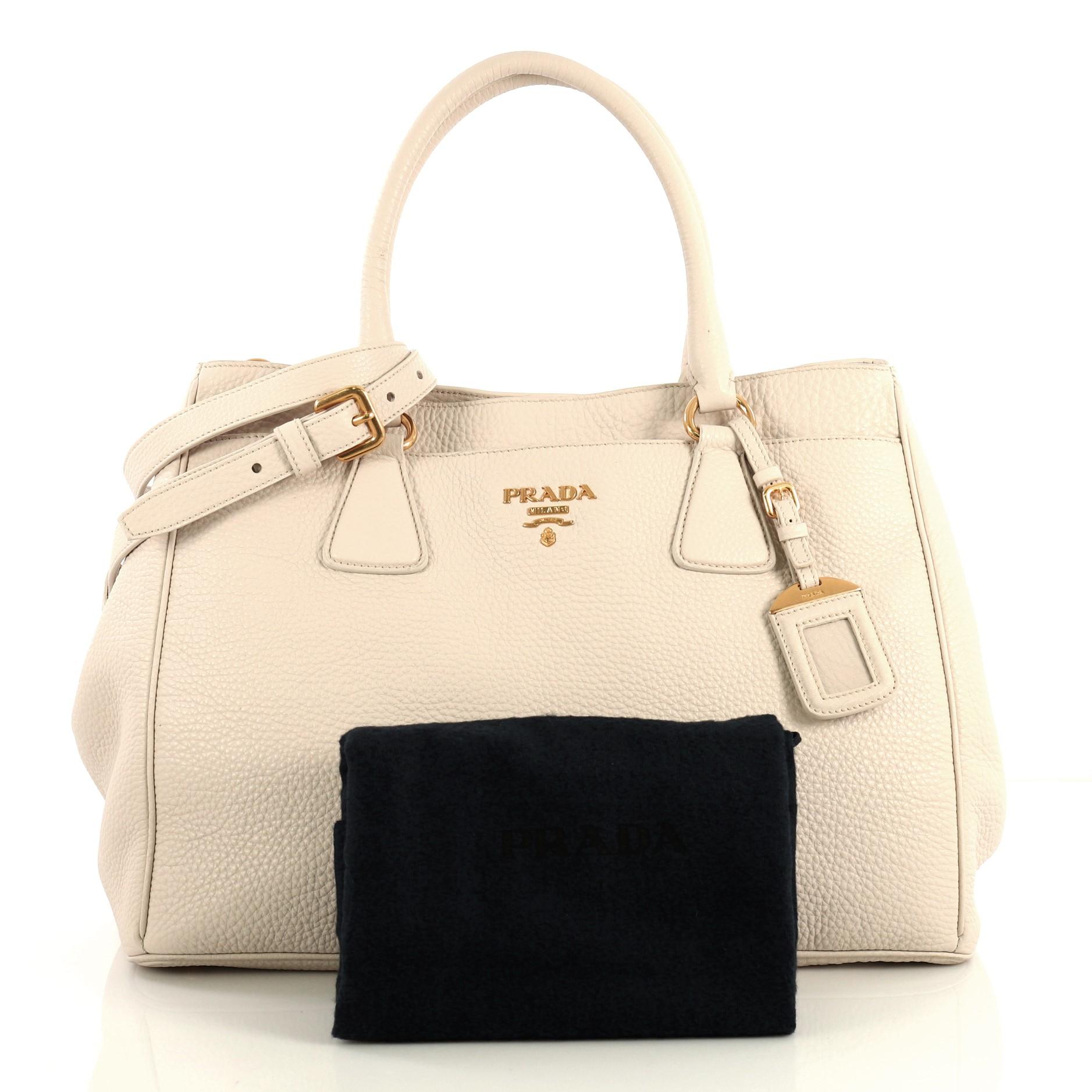 This Prada Convertible Shopping Tote Vitello Daino Large, crafted in neutral vitello daino leather, features dual rolled leather handles, Prada logo at the center, protective base studs, and gold-tone hardware. Its snap button closure opens to a