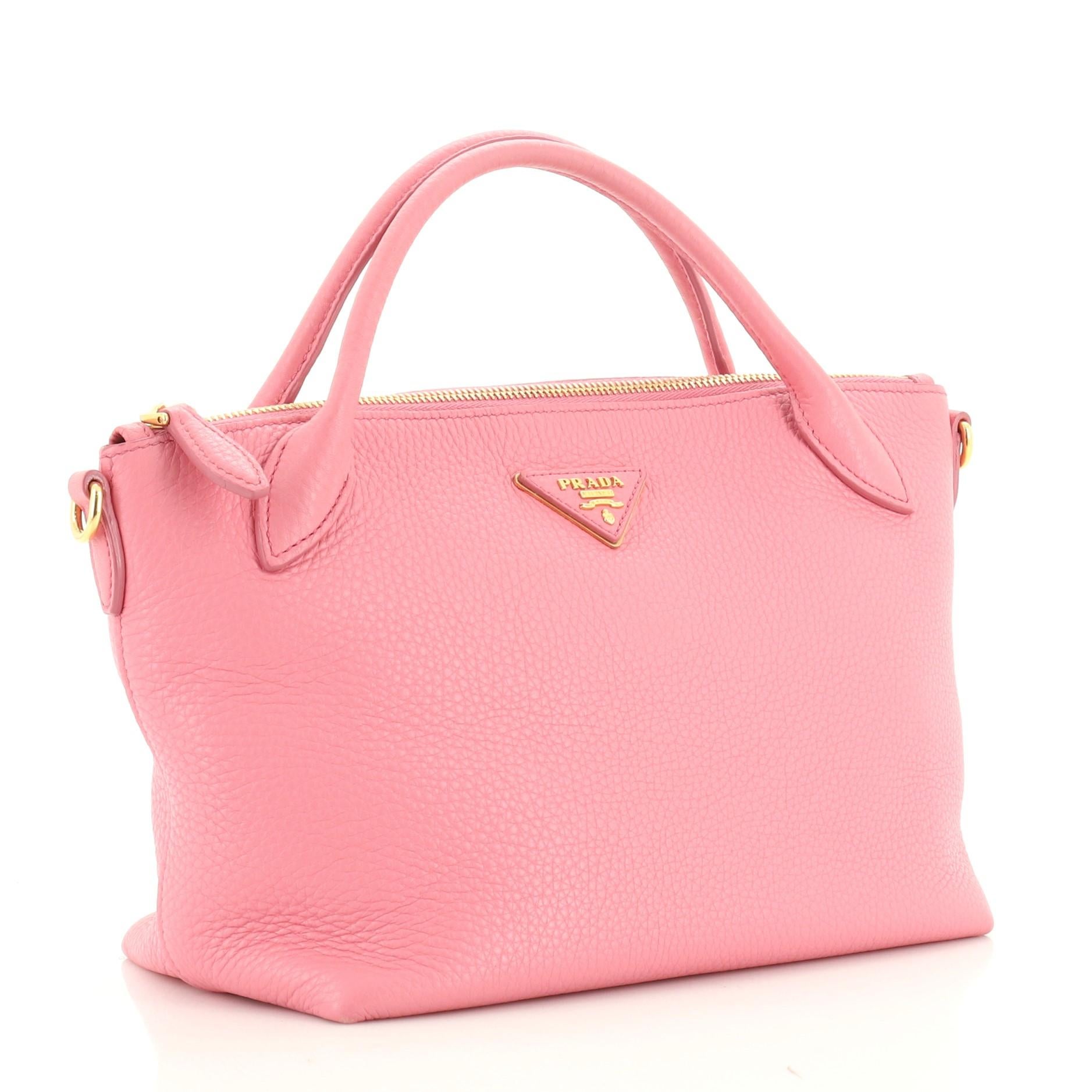 This Prada Convertible Top Handle Satchel Vitello Daino Small, crafted from pink vitello daino leather, features dual rolled leather handles, Prada Milano logo, and gold-tone hardware. Its top zip closure opens to a pink fabric interior with side