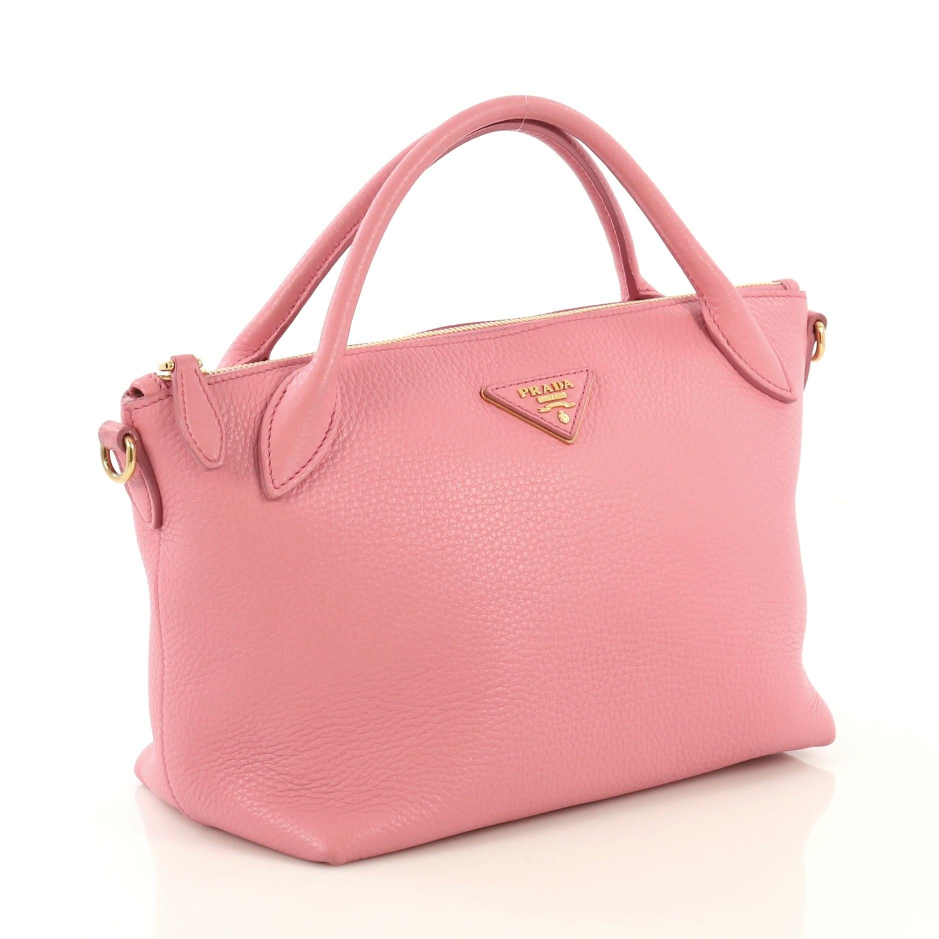 This Prada Convertible Top Handle Satchel Vitello Daino Small, crafted from pink vitello daino leather, features dual rolled leather handles, Prada Milano logo, and gold-tone hardware. Its top zip closure opens to a pink fabric and leather interior