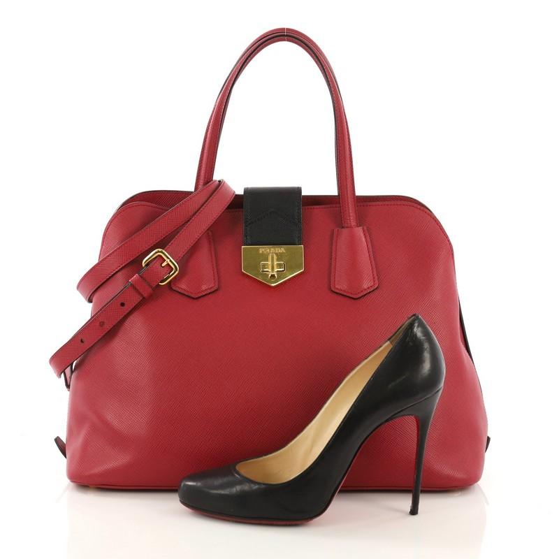 This Prada Convertible Turnlock Flap Promenade Handbag Saffiano Leather Medium, crafted in red saffiano leather, features dual leather handles, side snap buttons, protective base studs, and gold-tone hardware. Its flap tab with turn-lock closure
