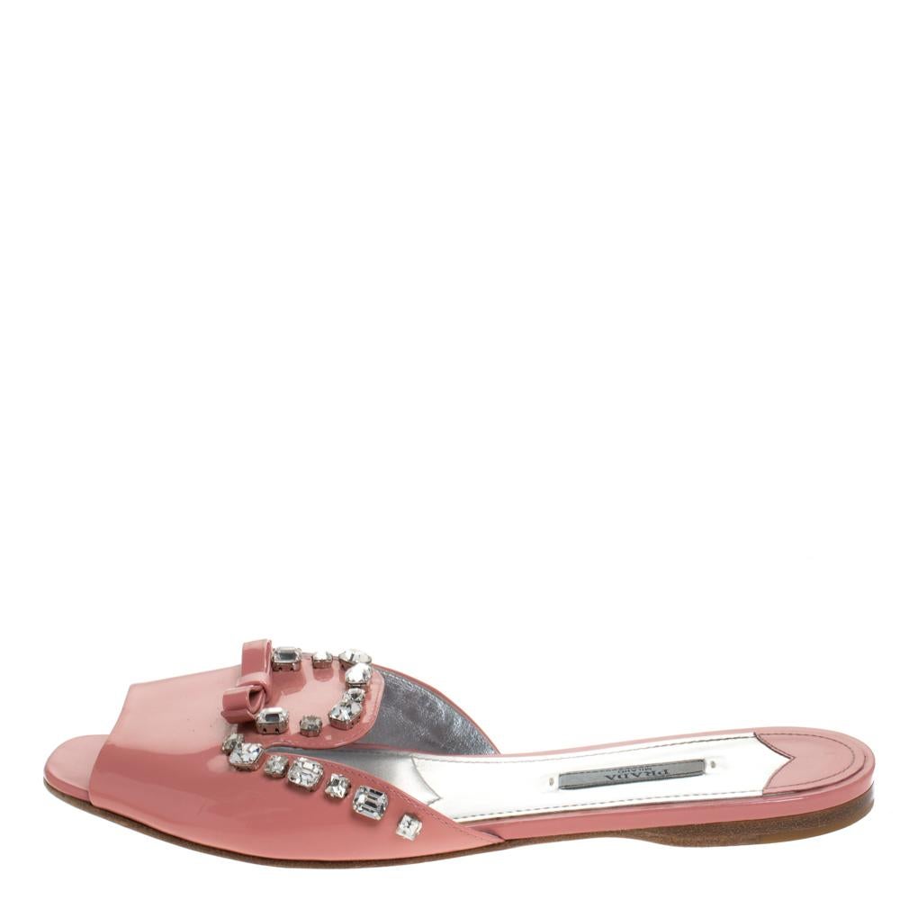 Amp up your casual style with these stunning flat slides from the house of Prada. Crafted in Italy, they are made from patent leather. They come in a pretty coral pink shade and are styled with open toes, broad vamp straps embellished with a bow and