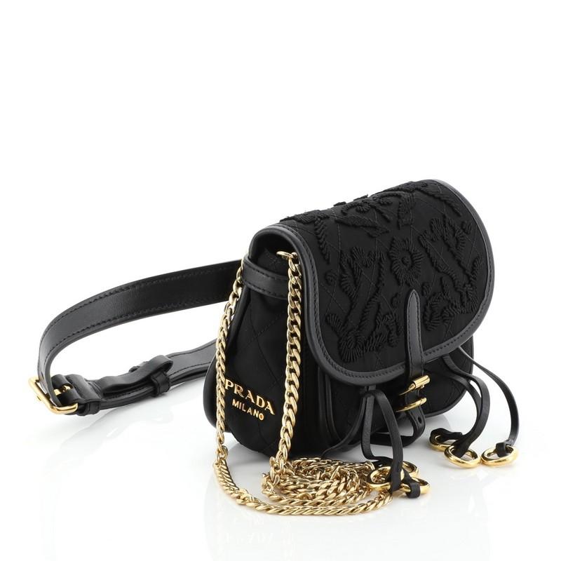 This Prada Corsaire Belt Bag Embroidered Quilted Tessuto Small, crafted in black nylon, features dual-rolled leather handles, detachable strap, and gold-tone hardware. Its zip closure opens to a black fabric and leather interior with side zip and