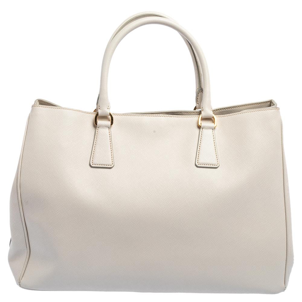 Loved for its classic appeal and functional design, Galleria is one of the most iconic and popular bags from the house of Prada. This beauty in cream is crafted from Saffiano leather and is equipped with two top handles, the brand logo at the front,