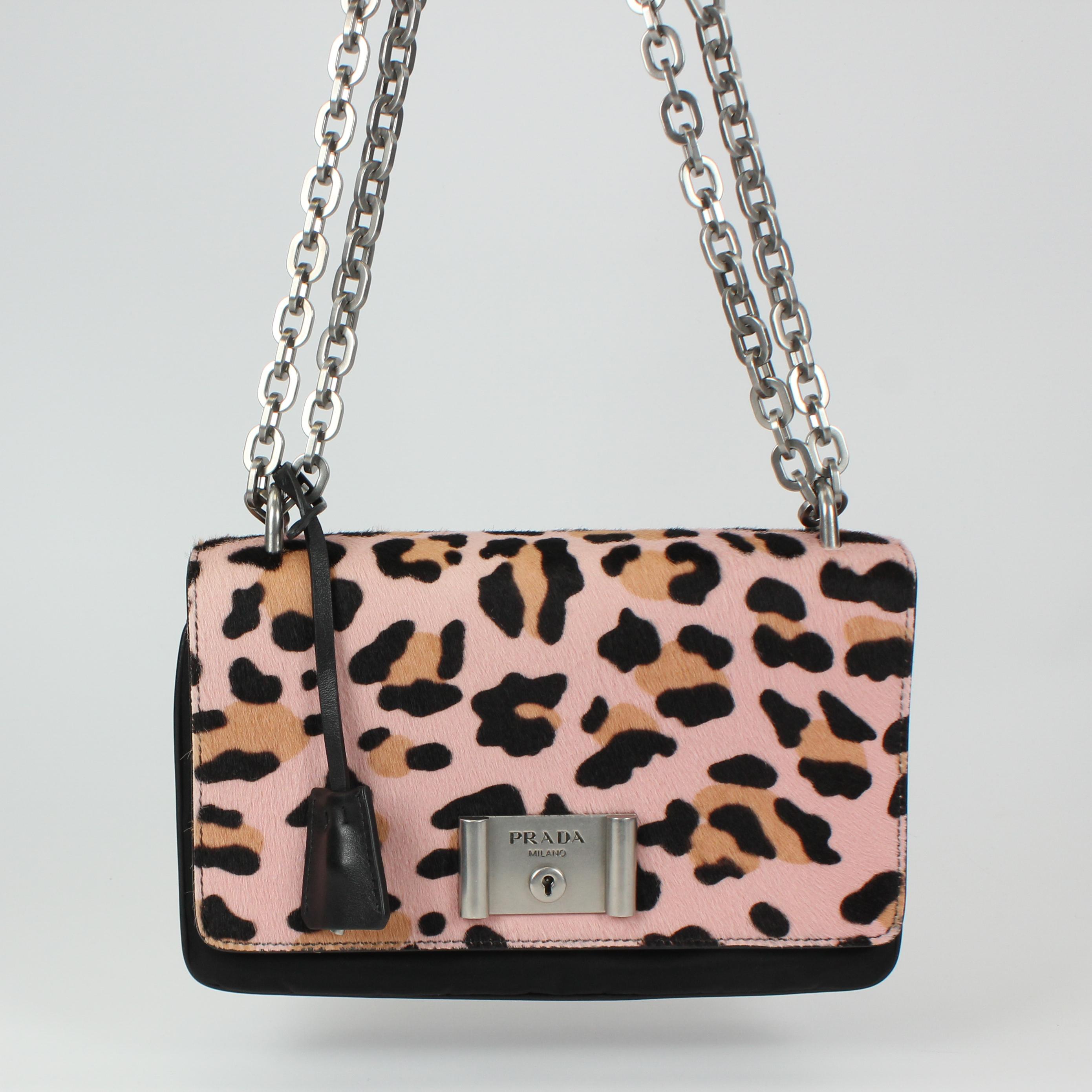 This Prada Pink Leopard Print Pony Hair and Nylon Chain Shoulder Bag 1BD009 features a chunky silvertone chain shoulder strap and a push-lock. Wear this with a colorful ensemble or stick to the all black and white trend for a crisp and modern
