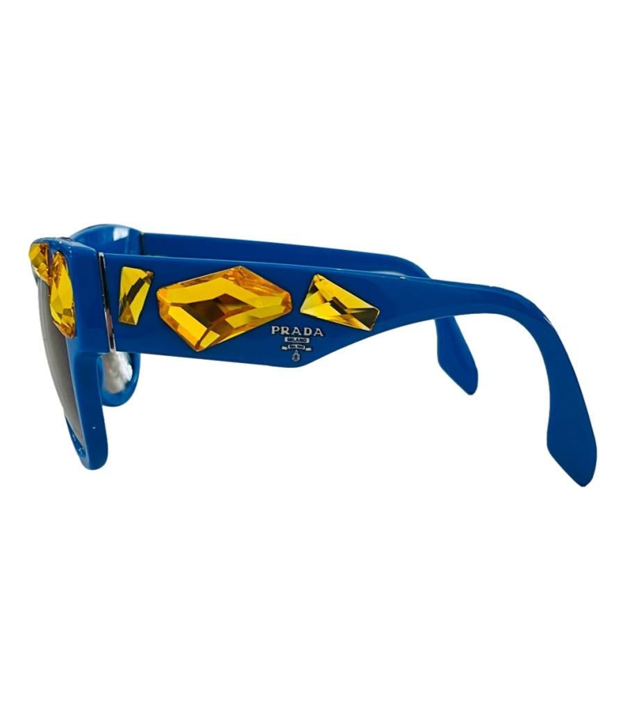 Prada Crystal Embellished Sunglasses
Blue cat-eye sunglasses designed with large yellow crystal embellishment to the frame and arms.
Detailed with silver 'Prada' logo to the side and brown gradient lenses.
Size – One Size
Condition – Very