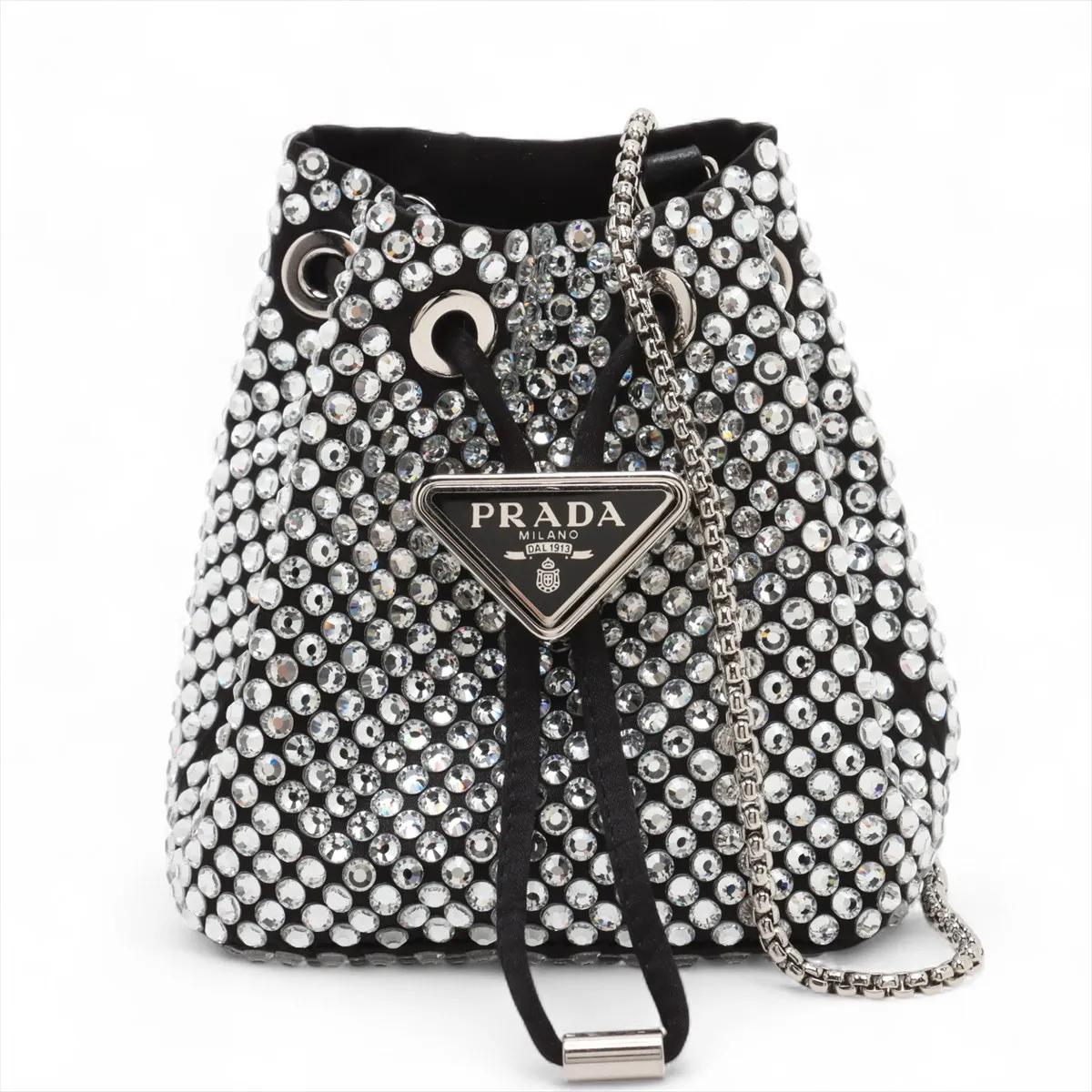 La borsa a tracolla Prada con cristalli e strass e catena di raso in nero e argento emana un fascino moderno e sofisticato. Realizzata in lussuoso raso e impreziosita da strass scintillanti, la borsa cattura la luce in modo meraviglioso, aggiungendo