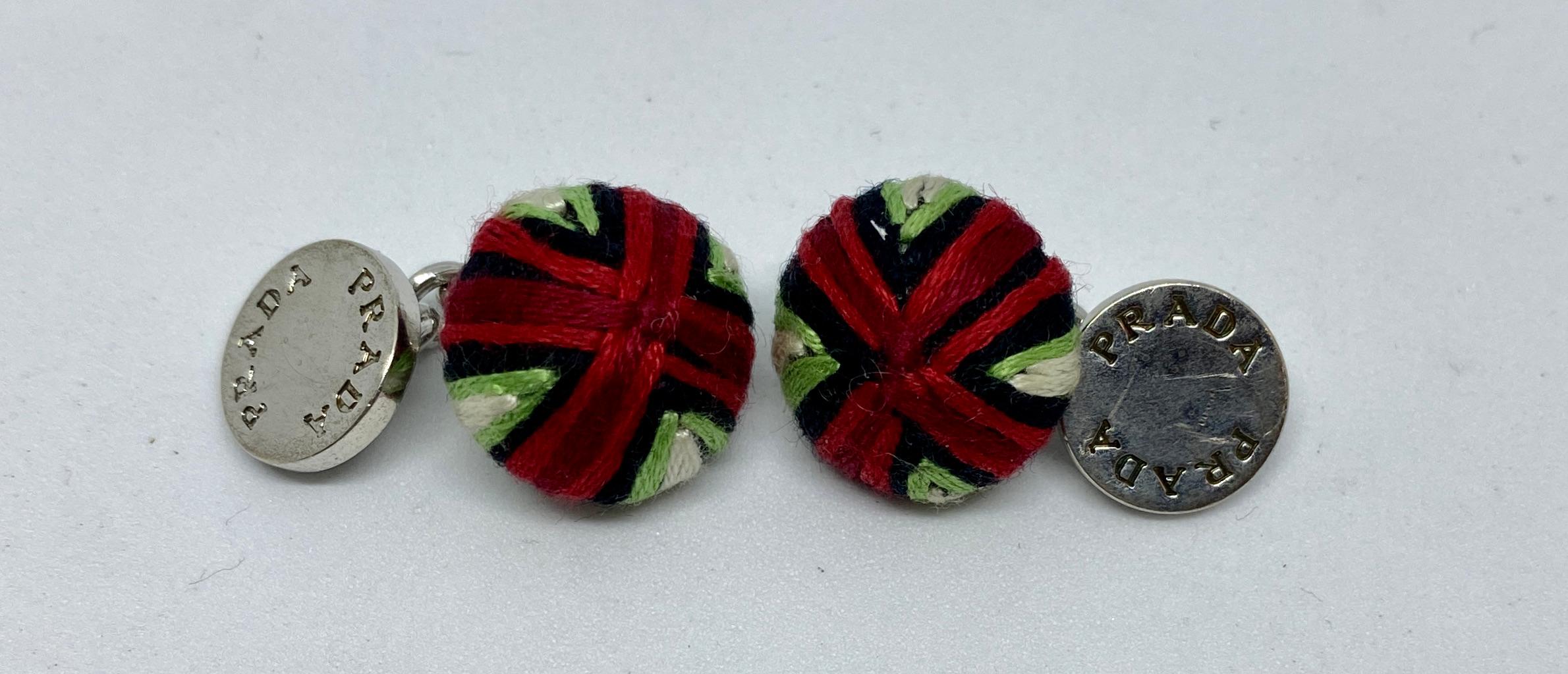 Highly original cufflinks in solid sterling silver with multicolored thread made to look like cloth buttons. 

The cufflink faces measure 15.7mm in diameter and feature an X pattern in dark and light red, black, green and white. The faces are