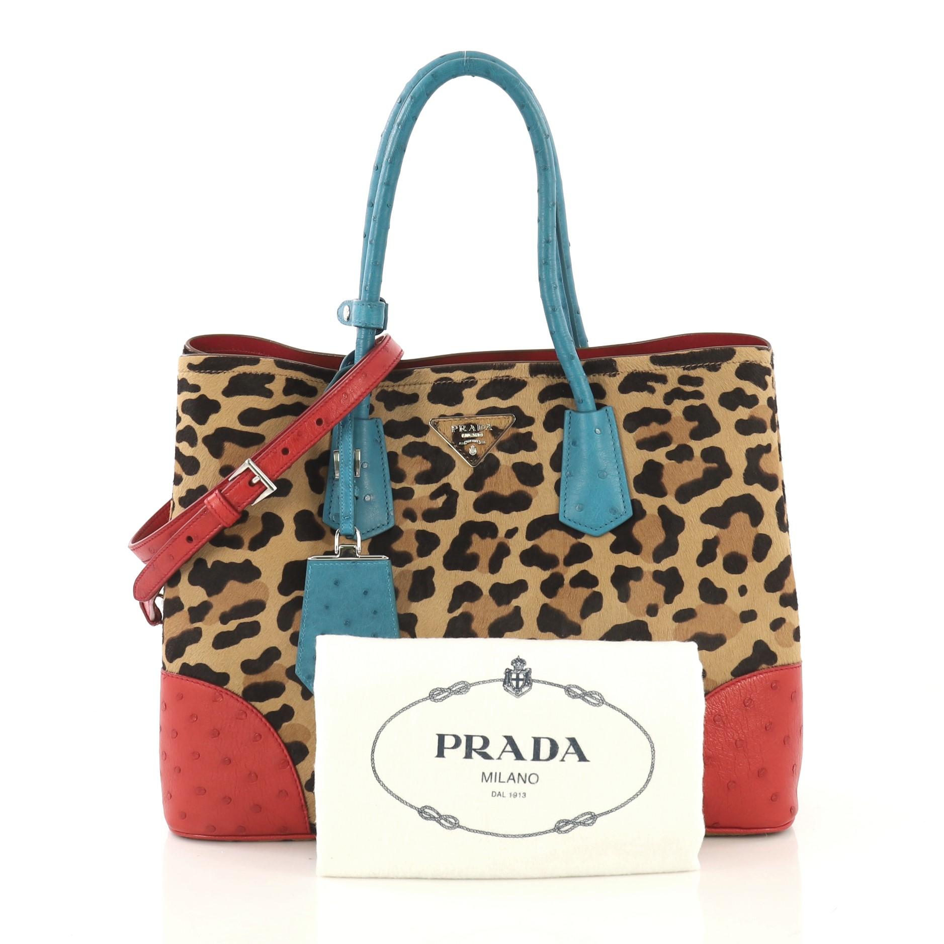 This Prada Cuir Double Tote Printed Calf Hair with Ostrich Medium, crafted from brown printed calf hair with genuine blue and red ostrich skin, features dual rolled handles, triangle logo at the center, and silver-tone hardware. It opens to a red