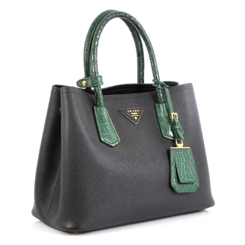 This Prada Cuir Double Tote Saffiano Leather and Crocodile Small, crafted from black saffiano leather and genuine crocodile skin, features dual rolled handles, triangle logo at the center, and gold-tone hardware. It opens to a black leather interior