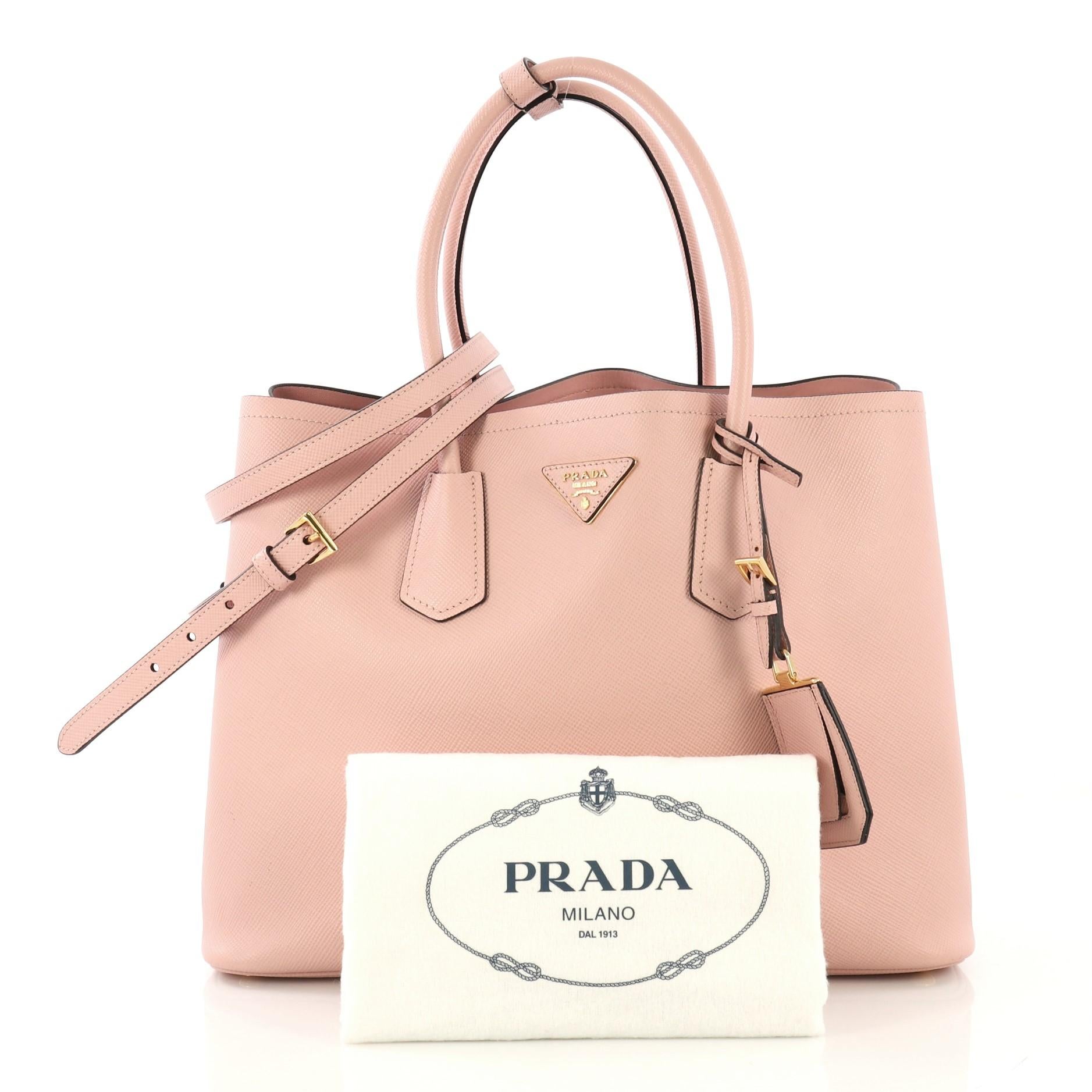 This Prada Cuir Double Tote Saffiano Leather Large, crafted from light pink saffiano leather, features dual rolled handles, triangle logo at the center, and gold-tone hardware. It opens to a pink leather interior with middle flap compartment.