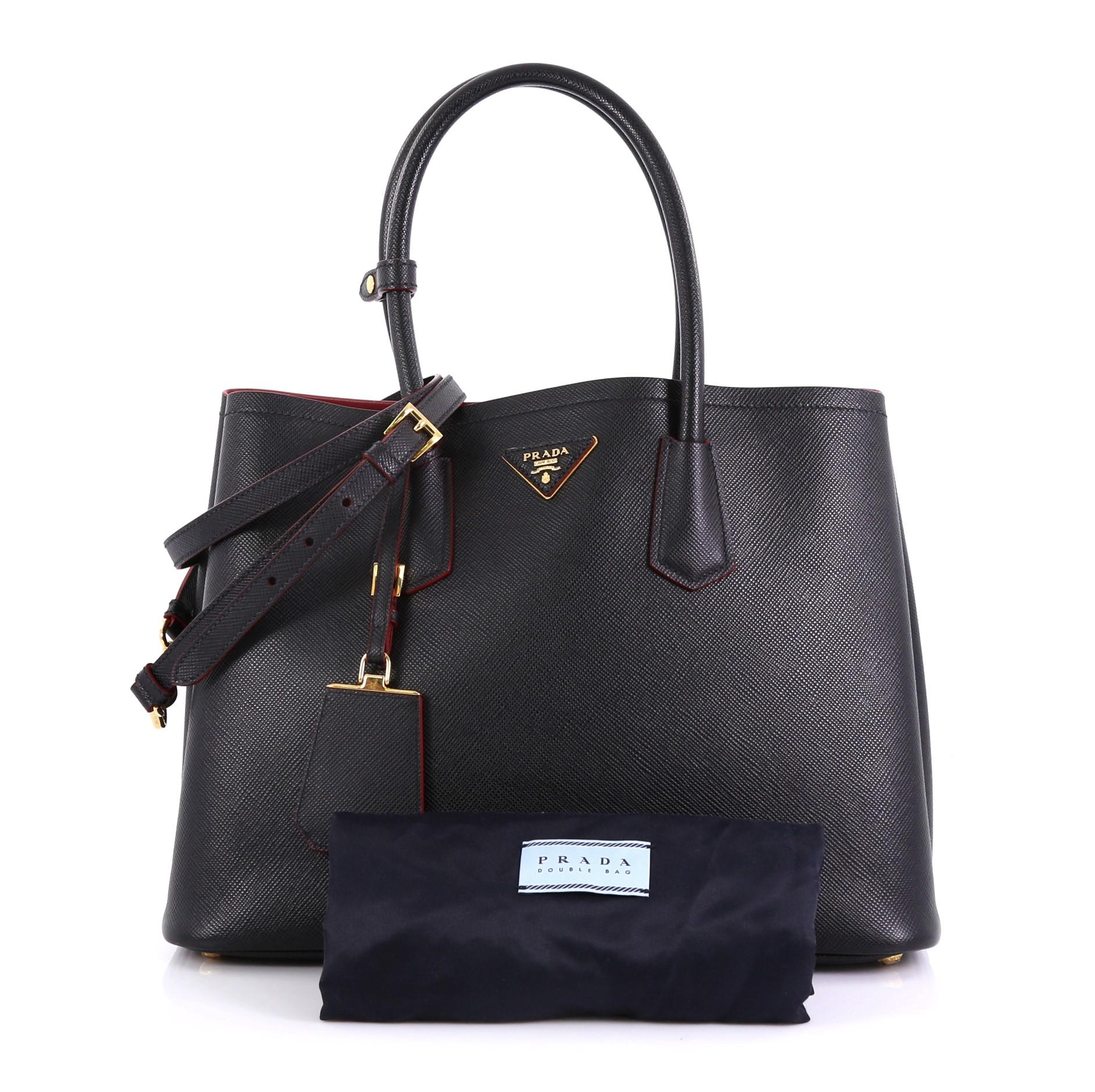 This Prada Cuir Double Tote Saffiano Leather Medium, crafted from black saffiano leather, features dual rolled handles, triangle logo at the center, and gold-tone hardware. It opens to a red leather interior with middle flap compartment. 

Estimated