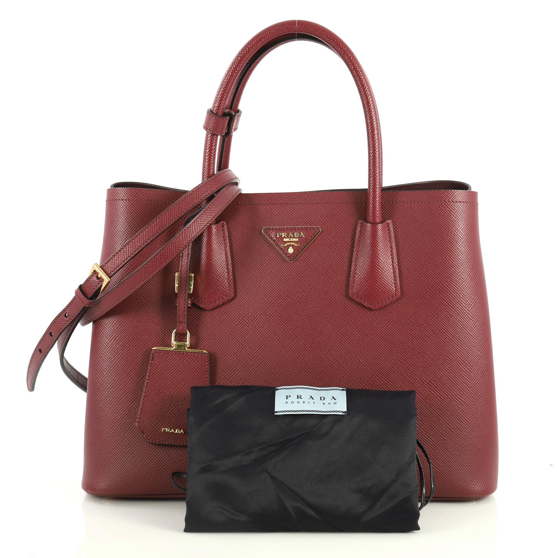 This Prada Cuir Double Tote Saffiano Leather Medium, crafted from red saffiano leather, features dual rolled handles, triangle logo at the center, and gold-tone hardware. It opens to a red leather interior with middle flap compartment. 

Estimated