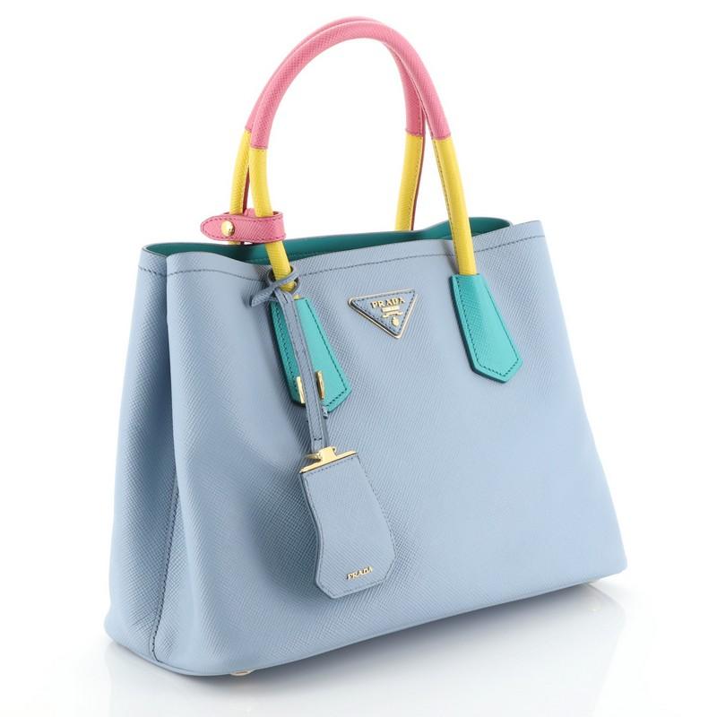 This Prada Cuir Double Tote Saffiano Leather Medium, crafted from blue and multicolor saffiano leather, features dual rolled handles, triangle logo at the center, and gold-tone hardware. It opens to a blue leather interior with middle flap