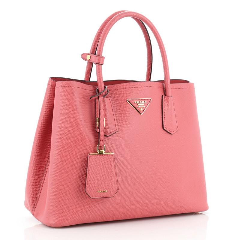 This Prada Cuir Double Tote Saffiano Leather Medium, crafted from pink saffiano leather, features dual rolled handles, triangle logo at the center, and gold-tone hardware. It opens to a pink leather interior with middle flap compartment. 

Estimated