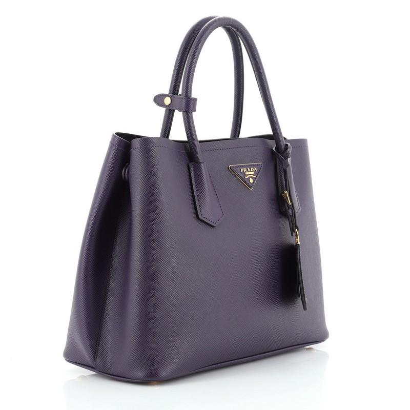 This Prada Cuir Double Tote Saffiano Leather Medium, crafted from purple saffiano leather, features dual rolled handles, triangle logo at the center, and gold-tone hardware. It opens to a black leather interior with middle flap compartment.