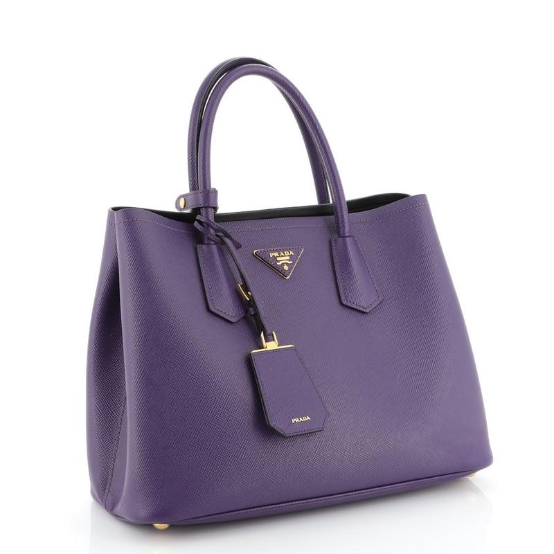 This Prada Cuir Double Tote Saffiano Leather Small, crafted from purple saffiano leather, features dual rolled handles, triangle logo at the center, and gold-tone hardware. It opens to a black leather interior with middle flap compartment.