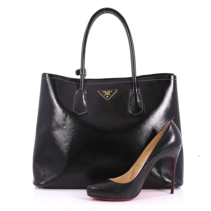 This Prada Cuir Double Tote Vernice Saffiano Leather Medium, crafted from black vernice saffiano leather, features dual rolled handles, side snap buttons, and gold-tone hardware. It opens to a black leather interior with middle flap compartment.