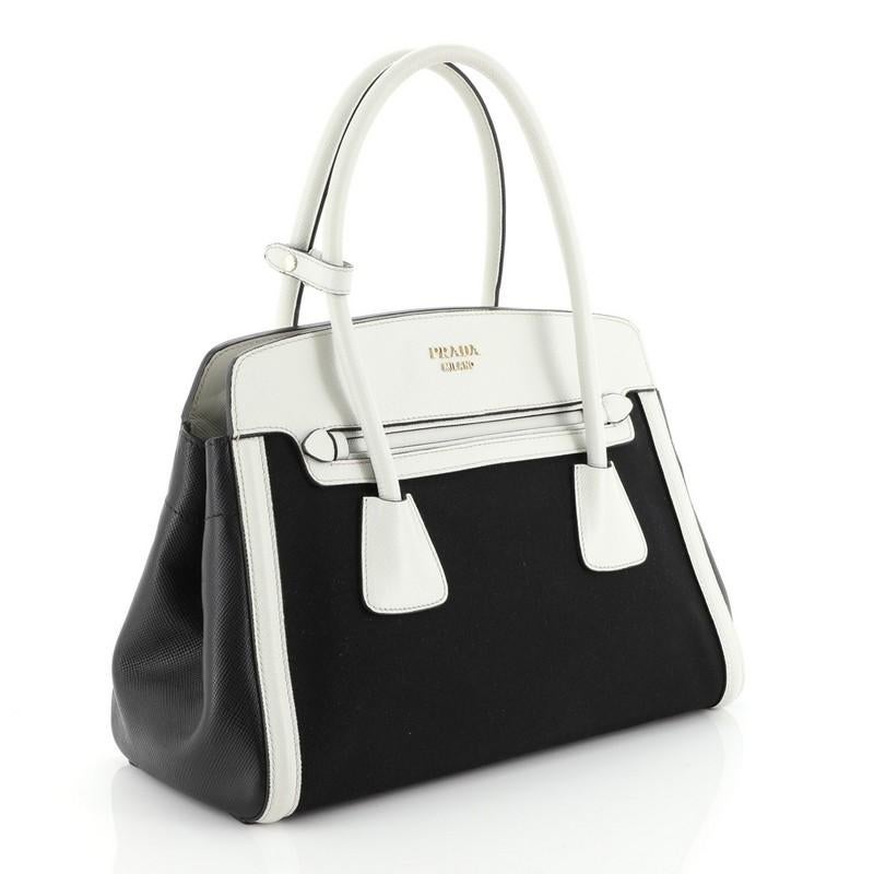 This Prada Cuir Frame Convertible Tote Canvas and Saffiano Leather Small, crafted in white leather and black canvas, features dual-rolled handles, side snap buttons, magnetic slip pockets in front and gold-tone hardware. Its snap closure opens to a