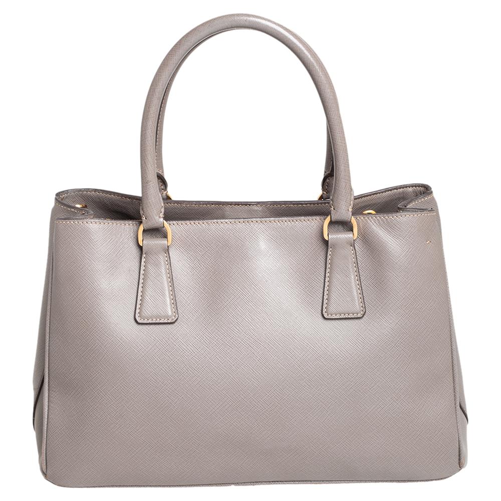 Prada's finest range of totes includes this beauty here. It is crafted in a signature structured silhouette using dark beige Saffiano Lux leather and held by two top handles and a detachable shoulder strap. The designer tote is lined with nylon and