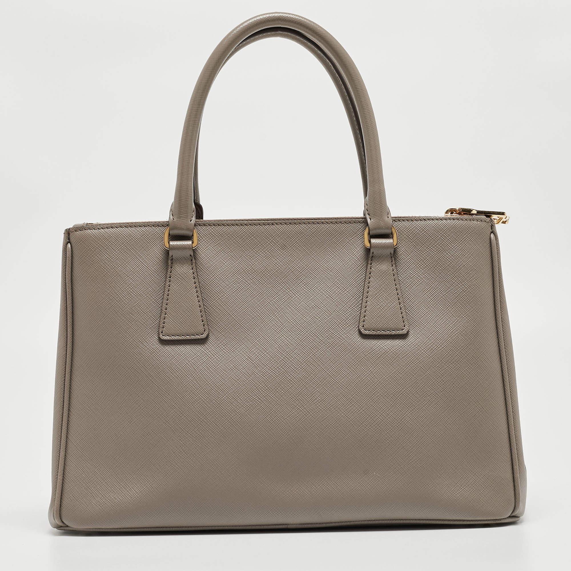 Loved for its classic appeal and functional design, Galleria is one of the most iconic and popular bags from the house of Prada. This beauty in dark beige is crafted from Saffiano Lux leather and is equipped with two top handles, the brand logo at