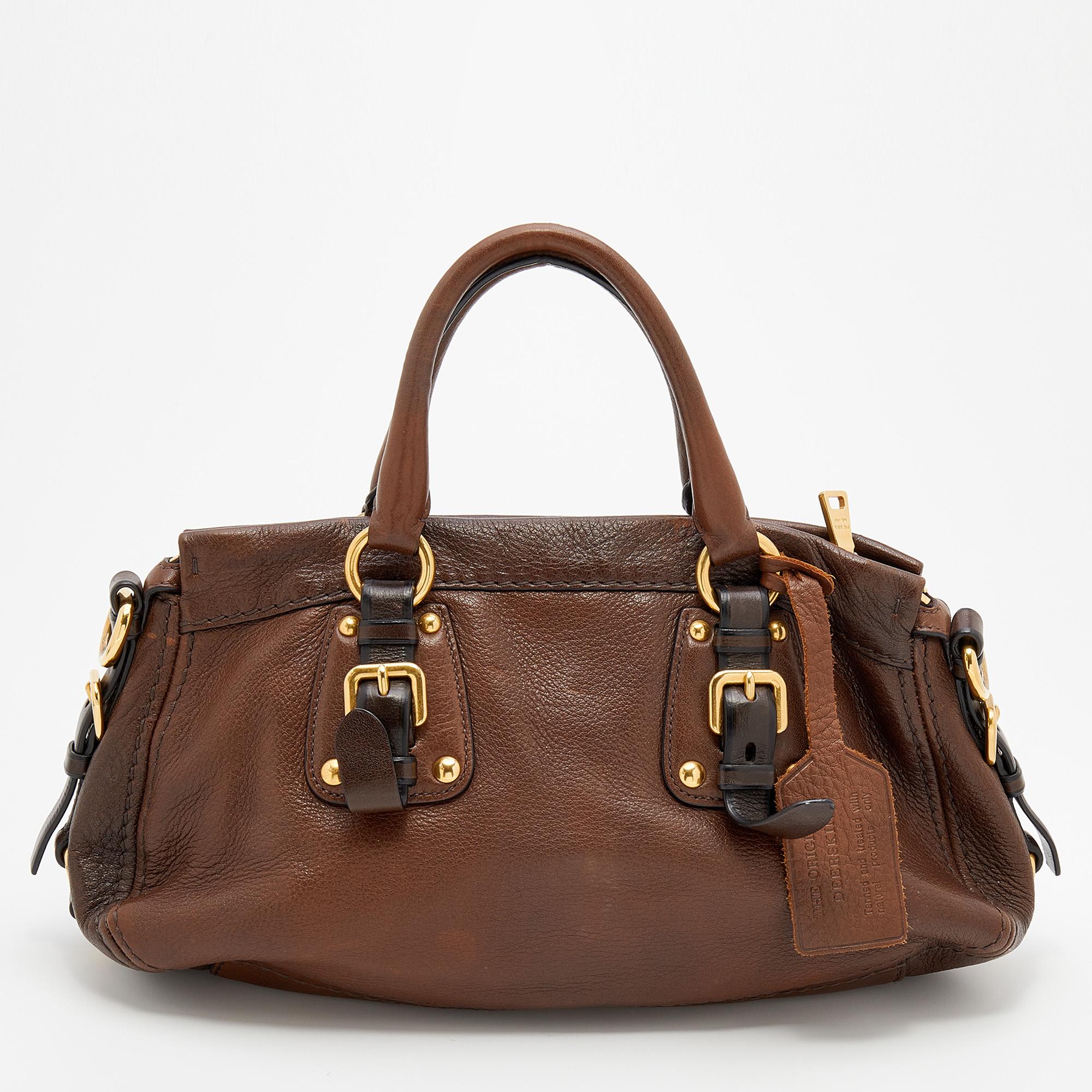 Carry this chic satchel from Prada for all your casual outings! It is made from leather and features a classic dark brown shade with gold-tone hardware. It is complete with dual handles, a shoulder strap, and a spacious interior for your