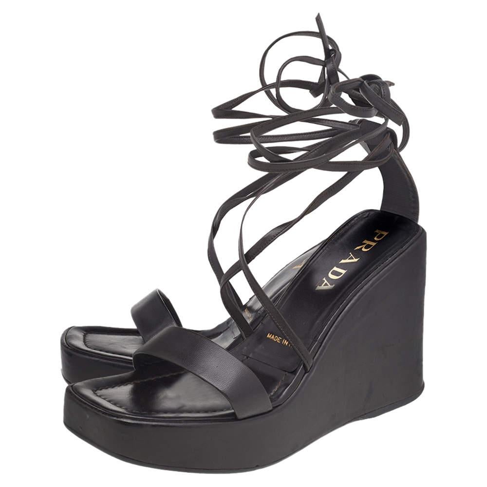 A feminine flair, sleek cuts, and a timeless appeal characterize these stunning Prada sandals. Crafted from dark brown leather, they are adorned with open toes and raised on high heels supported by platforms.

