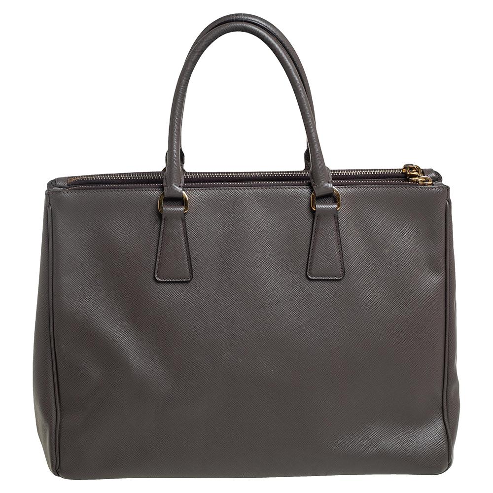Loved for its classic appeal and functional design, Galleria is one of the most iconic and popular bags from the house of Prada. This beauty in dark grey is crafted from Saffiano Lux leather and is equipped with two top handles, the brand logo at