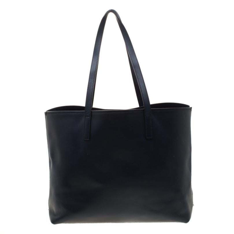 This shopper tote from Prada is a timeless piece. The bag comes in a luxurious dark navy blue leather exterior with silver-tone hardware. It features dual top handle straps with an attached tag accent and the brand logo at the front with a slip