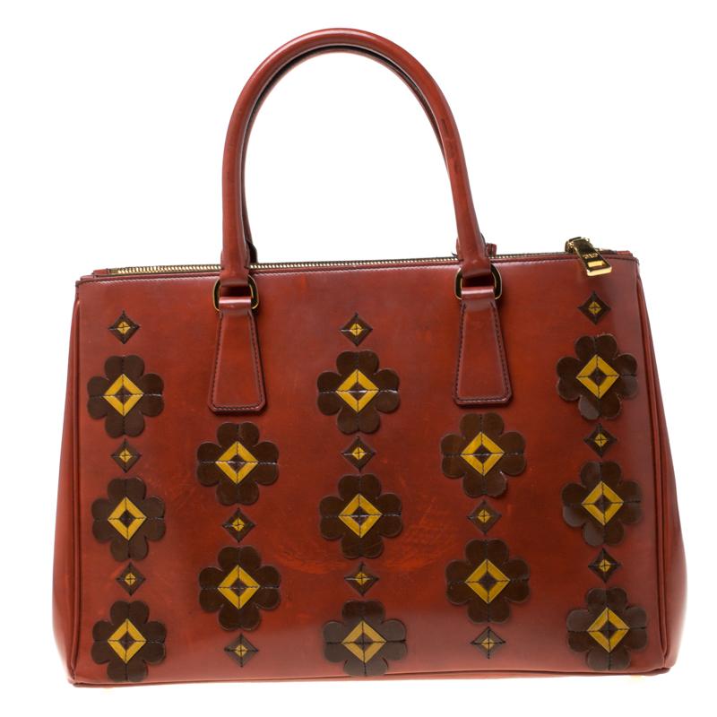 Feminine in shape and grand on design, this Double Zip tote by Prada will be a loved addition to your closet. It has been crafted from leather and styled with floral appliques all over the exterior along with gold-tone hardware. It comes with two