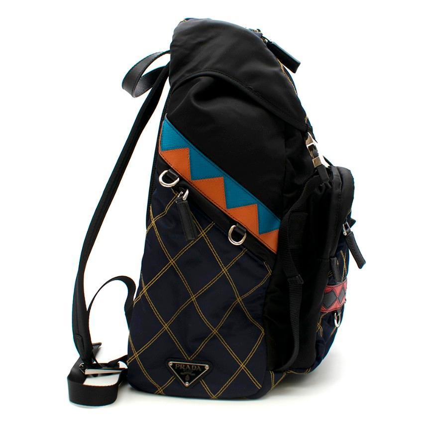 Prada Patterned Black/Blue Nylon & Leather Backpack.

- Crafted of navy and black quilted tech fabric
- Detailed with multicoloured leather in geometrical shapes on front and sides
- Metal logo at side
- Flap with side release buckles
- Four