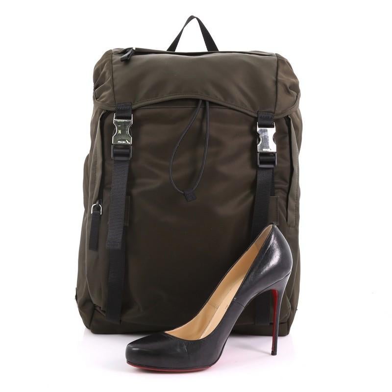 This Prada Double Buckle Backpack Tessuto, crafted in olive green tessuto, features a top carry handle, adjustable back shoulder straps, double-buckle flap, two exterior front zip pockets, and silver-tone hardware. Its drawstring closure opens to a