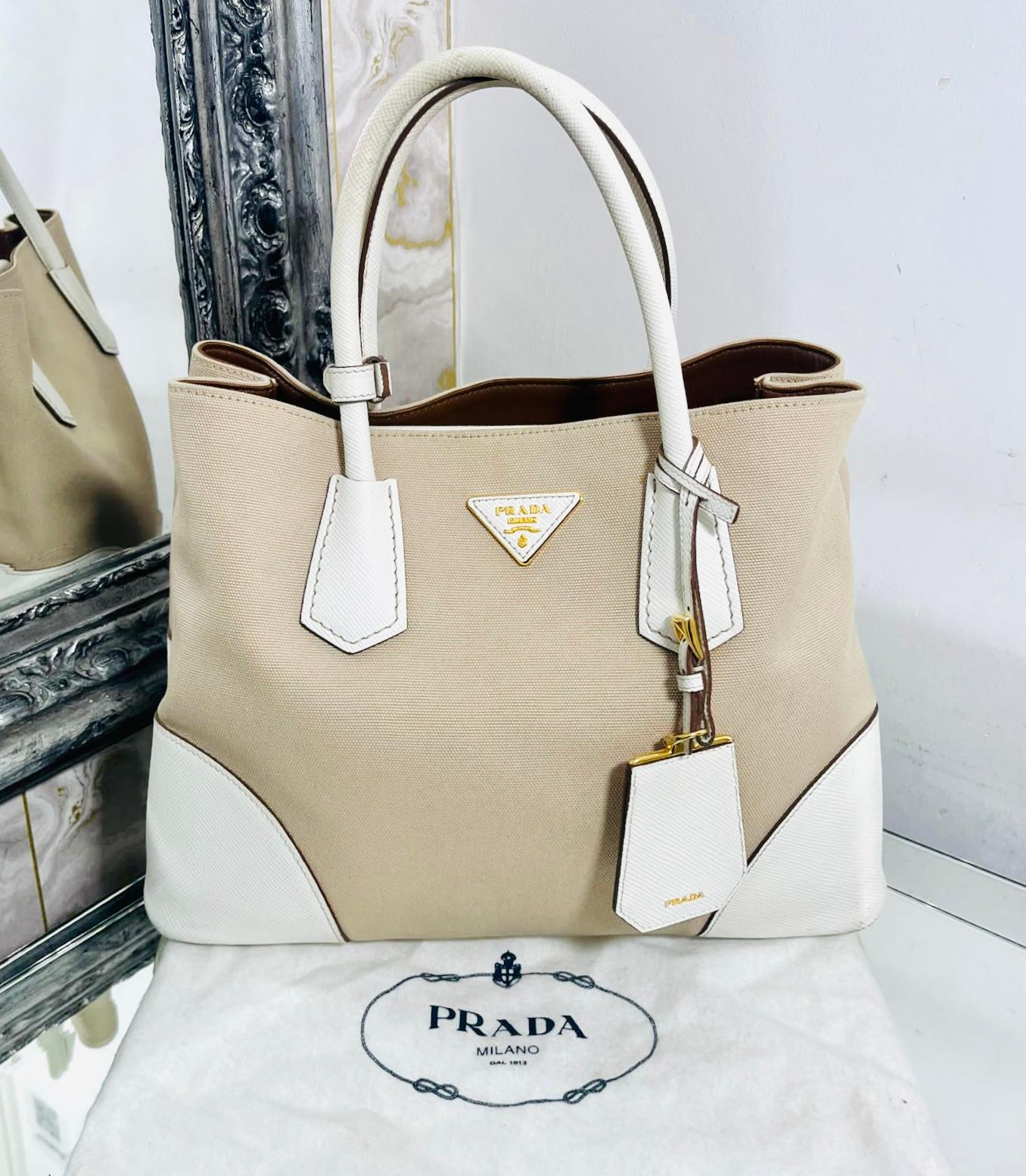 Prada Double Cuir Saffiano Leather & Canvas Tote Bag

Beige handbag designed with white leather corners and rolled top handles.

Detailed with signature gold  'Prada' logo engraved triangle and white leather name tag.

Featuring leather lining with