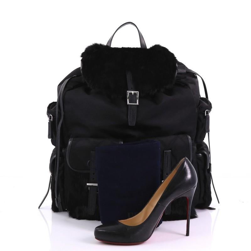This Prada Double Front Pocket Backpack Tessuto with Fur Medium, crafted in black tessuto with fur, features a top carry handle, adjustable shoulder straps, buckled fur flap, two exterior front zip pockets, and silver-tone hardware. Its drawstring