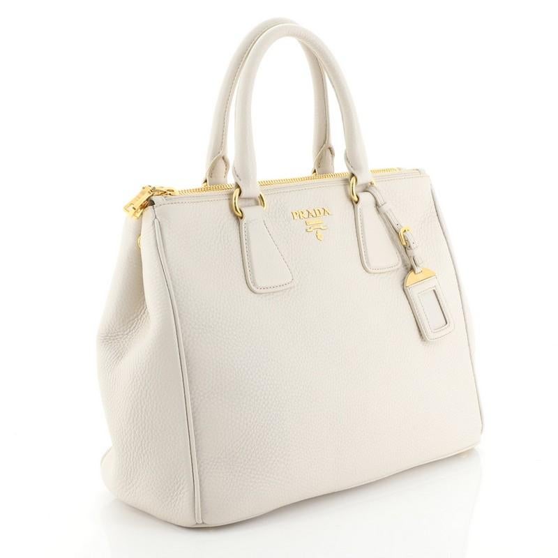 This Prada Double Zip Convertible Tote Vitello Daino Large, crafted in neutral vitello daino leather, features dual rolled leather handles, side snap buttons, raised Prada logo, and gold-tone hardware. It opens to a neutral fabric interior with side