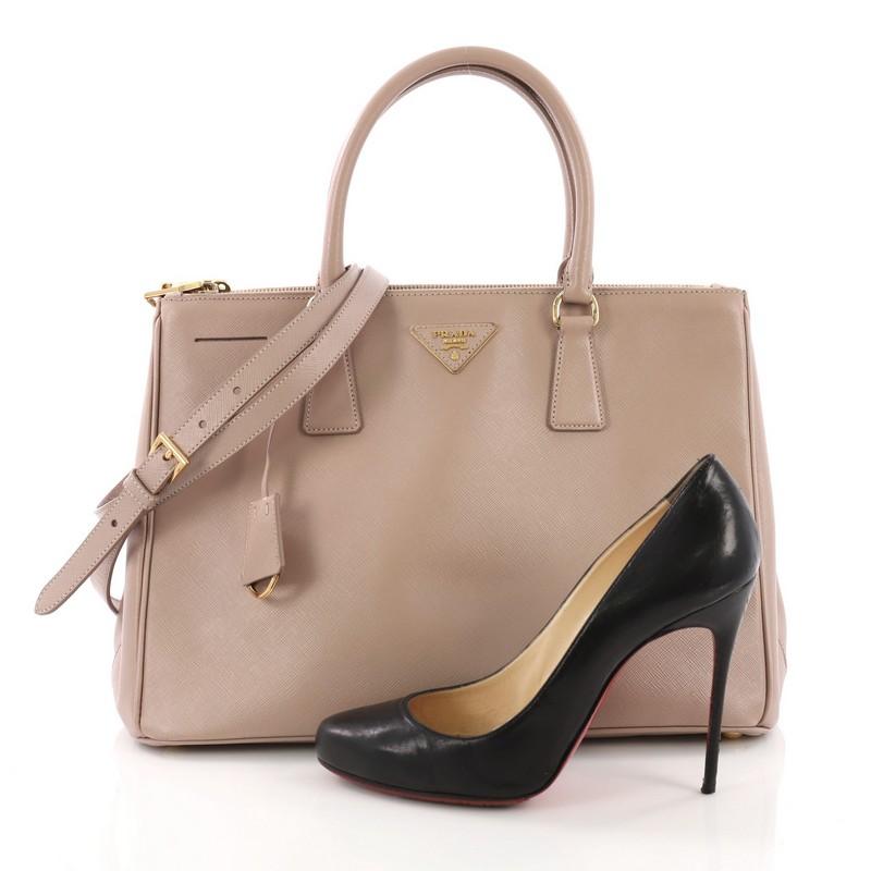 This Prada Double Zip Lux Tote Saffiano Leather Medium, crafted from light pink saffiano leather, features dual rolled handles, raised Prada logo plate, and gold-tone hardware. It opens to a beige fabric interior with two zip compartments on both